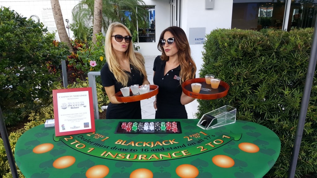 ladies in sunglasses with drink trays standing behind blackjack table at a charity event