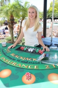 Female card dealer at outdoor event behind black jack table near swimming pool